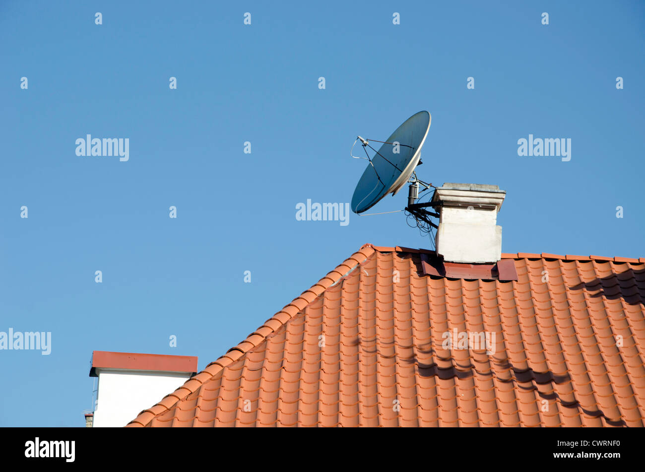 Satelliten-TV-Antenne angeschlossen an Schornstein auf rotem Ziegeldach Haus im Hintergrund des blauen Himmels. Stockfoto