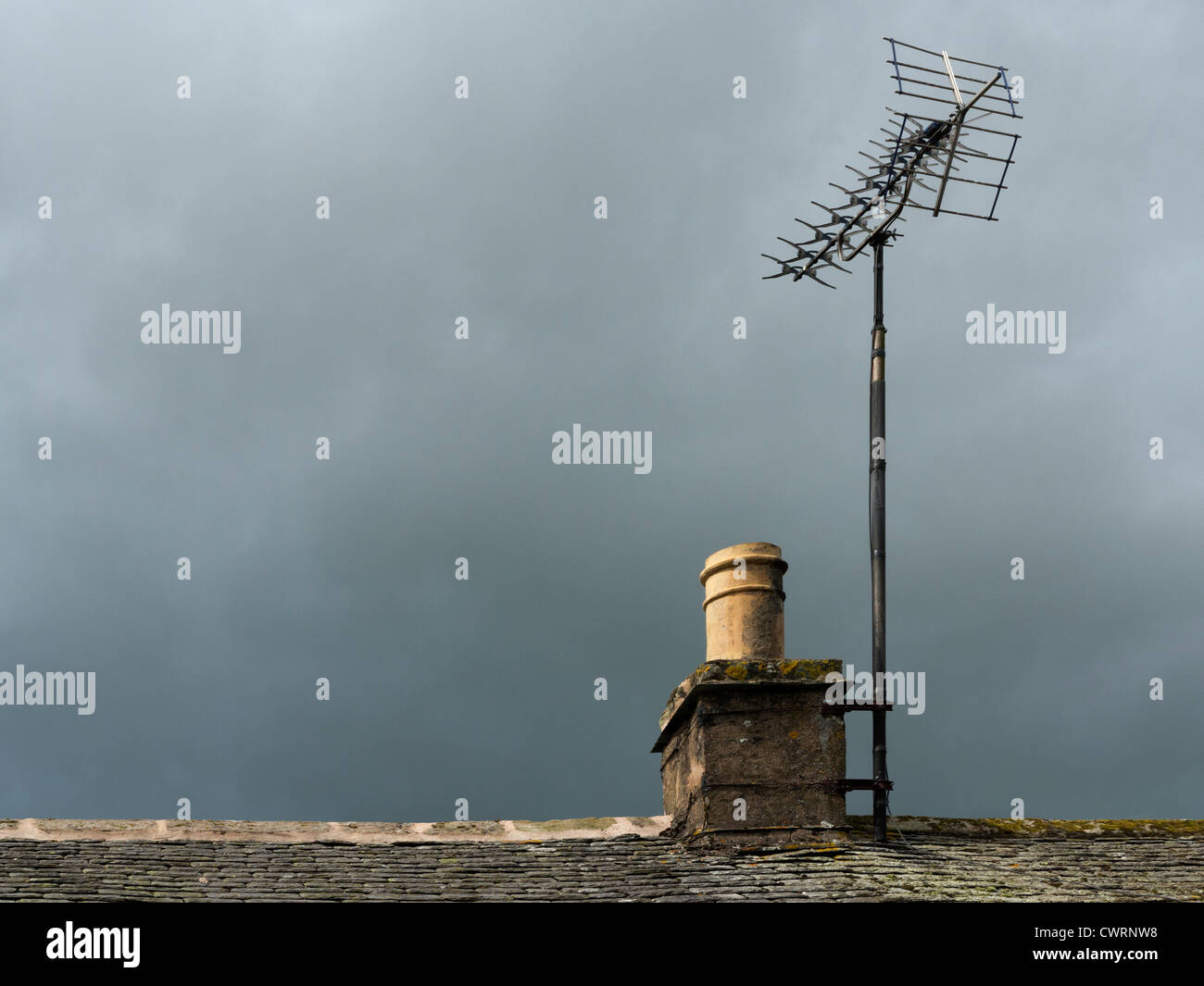 Landhaus Stein Kamin und Teil der Schieferdach mit TV Antenne vor einem dunklen grüblerischen Himmel Stockfoto