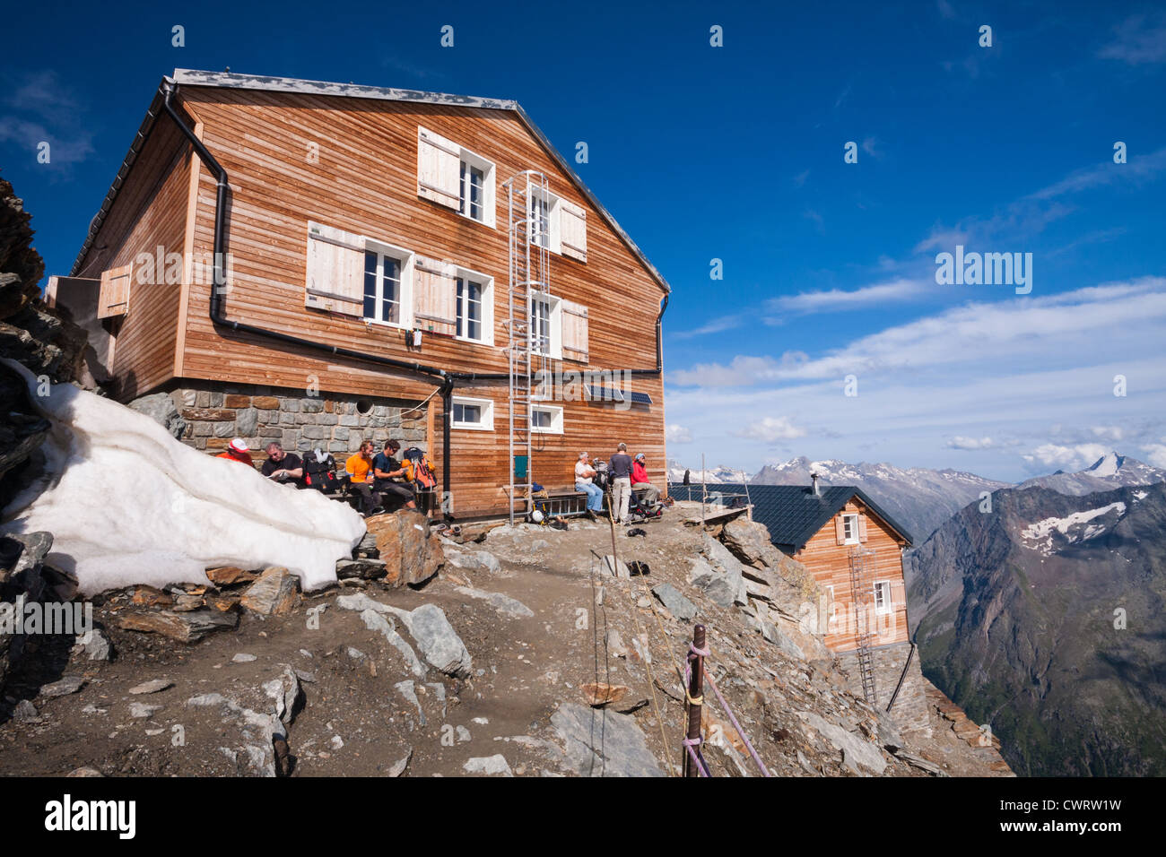 Bergsteiger ruhen Sie sich in der wärmenden Sonne am Nachmittag außerhalb der Mischabel-Hütte oberhalb von Saas-Fee in den Schweizer Alpen. Stockfoto