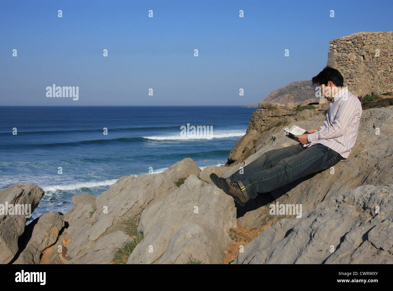 Junger Mann, ein Buch auf einem Felsen mit einem tollen Blick über das Meer Stockfoto