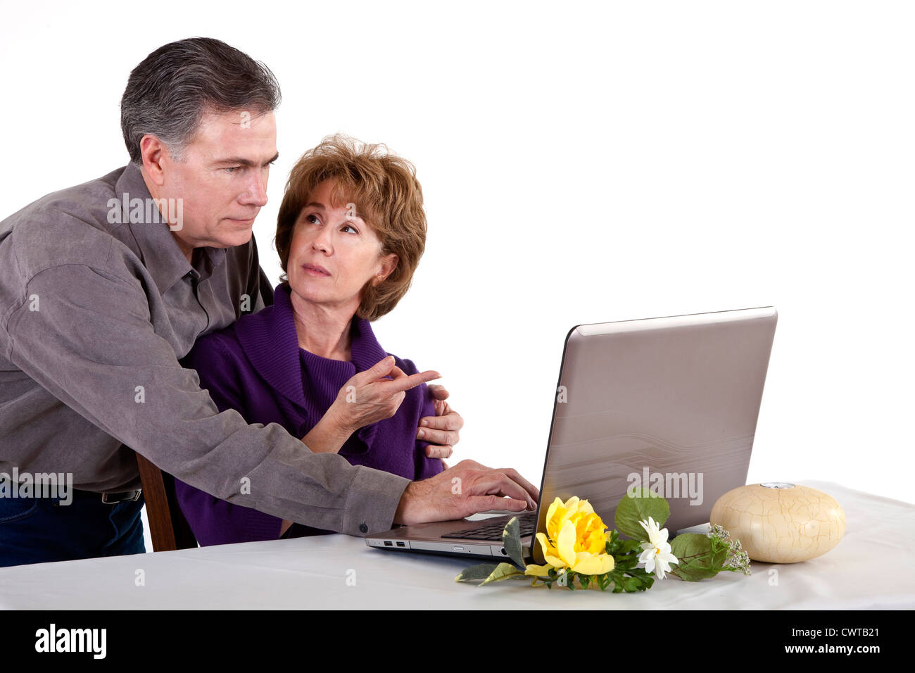 Eine reife Frau mit einem erstaunten Blick auf ihrem Gesicht mit ihrem Computer von ihrem Mann unterstützt. Stockfoto