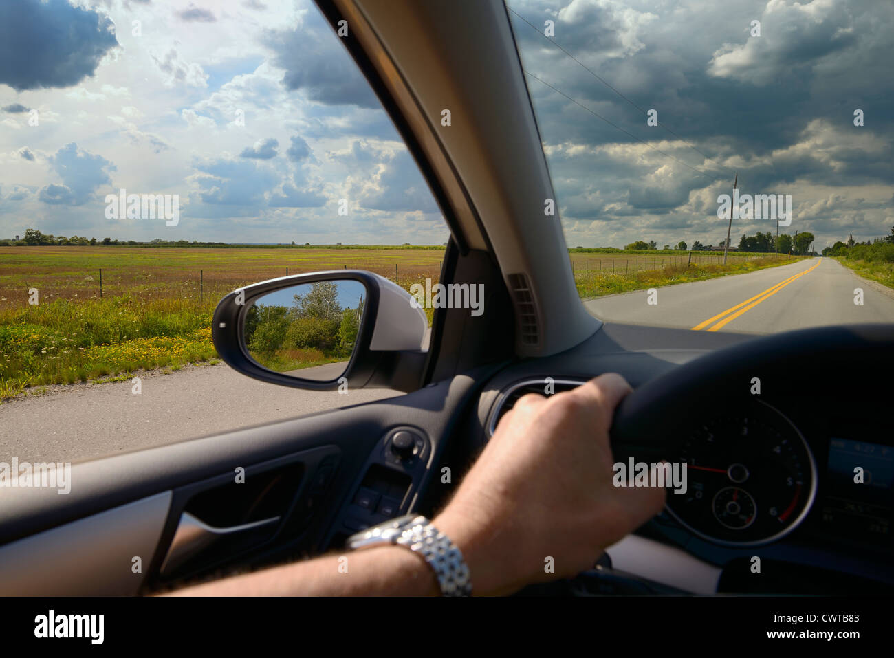 Mann mit der Hand am Lenkrad des Autos fahren mit offenen Fenster eine Landstraße mit Wolken von Ontario, Kanada Stockfoto