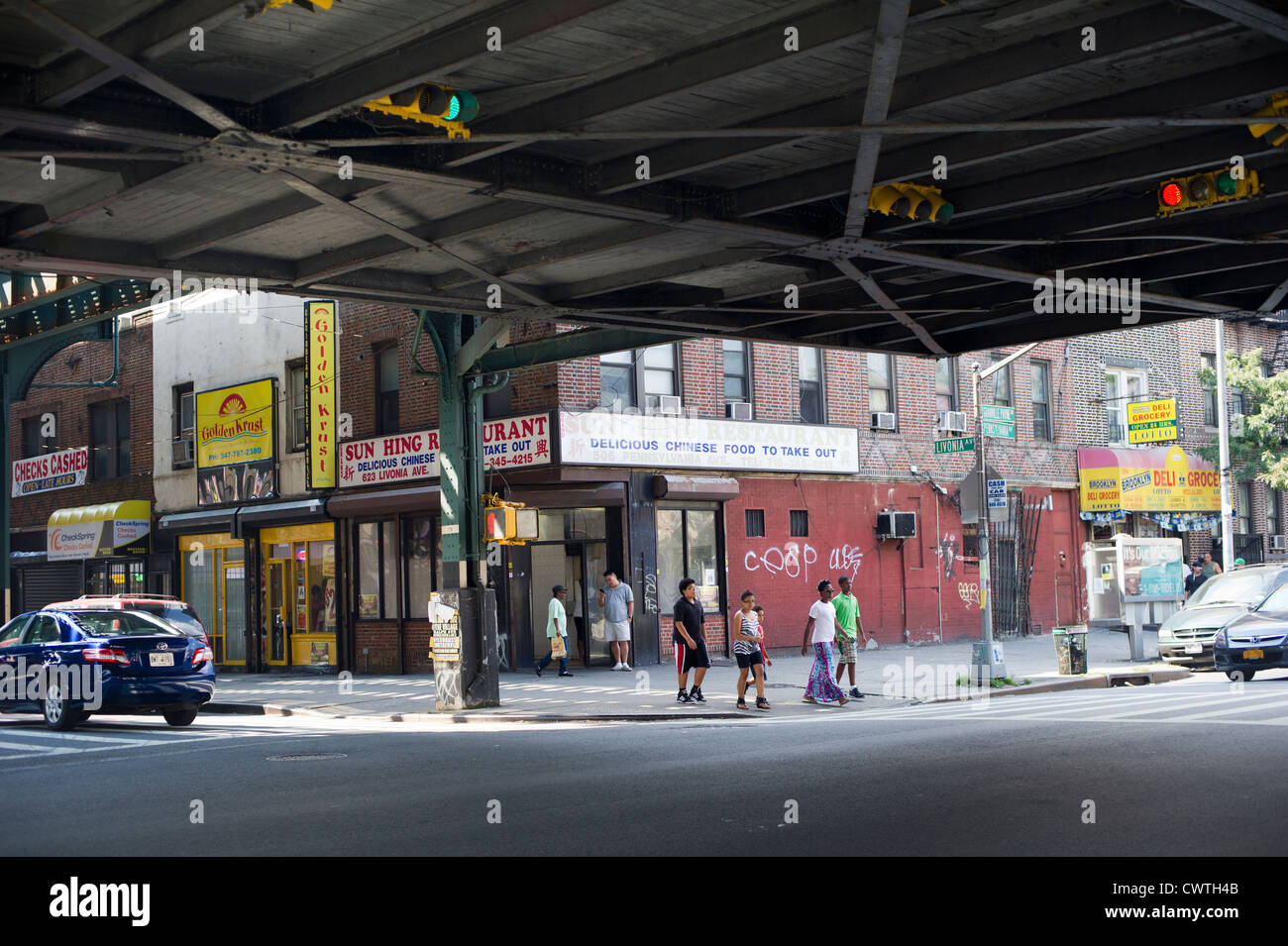 Fußgänger überqueren Sie die Straße unter der erhöhten u-Bahn-Gleise im Stadtteil East New York Brooklyn in New York Stockfoto