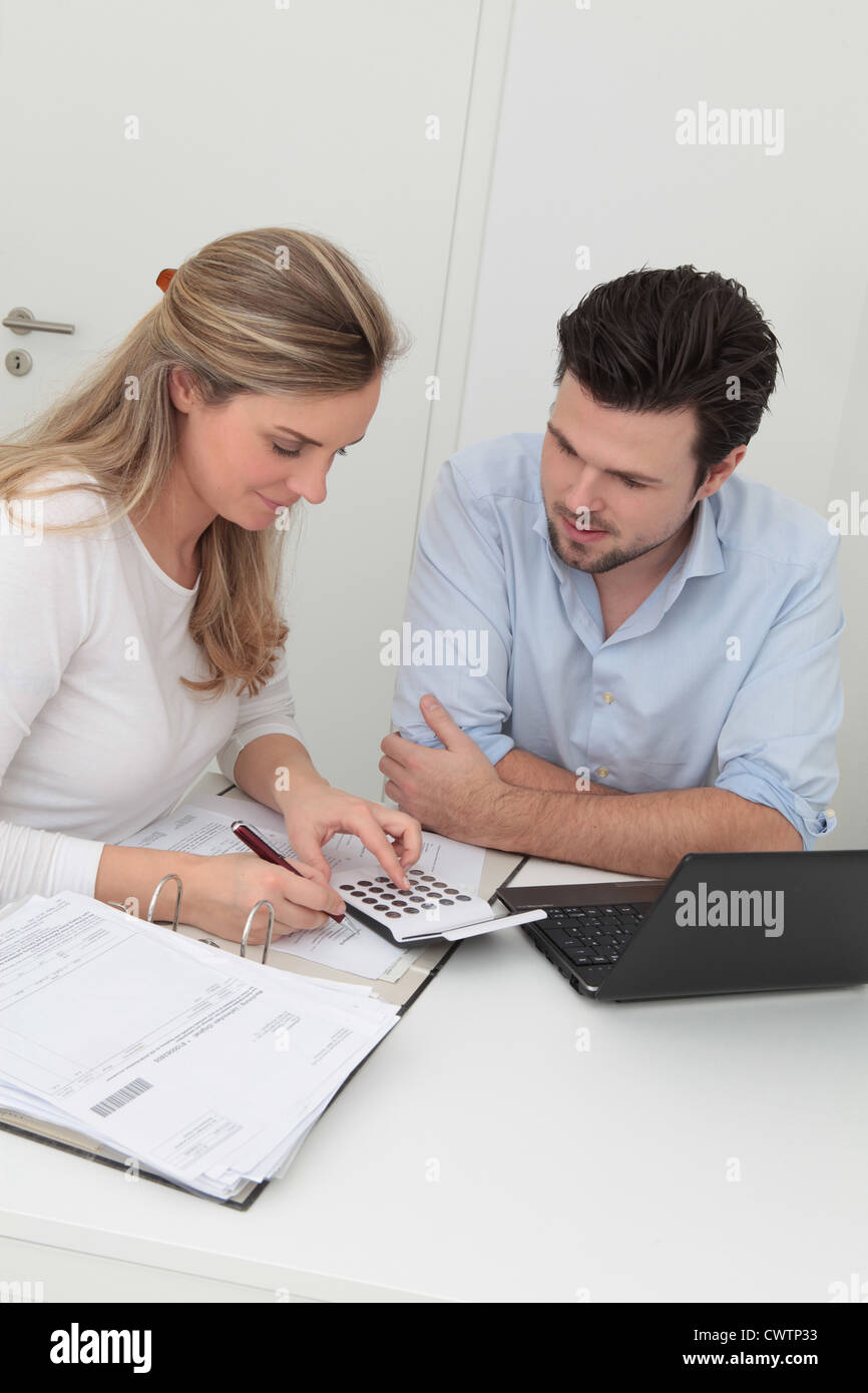 Mann und Frau sitzen am Tisch mit Datei, Rechner und laptop Stockfoto