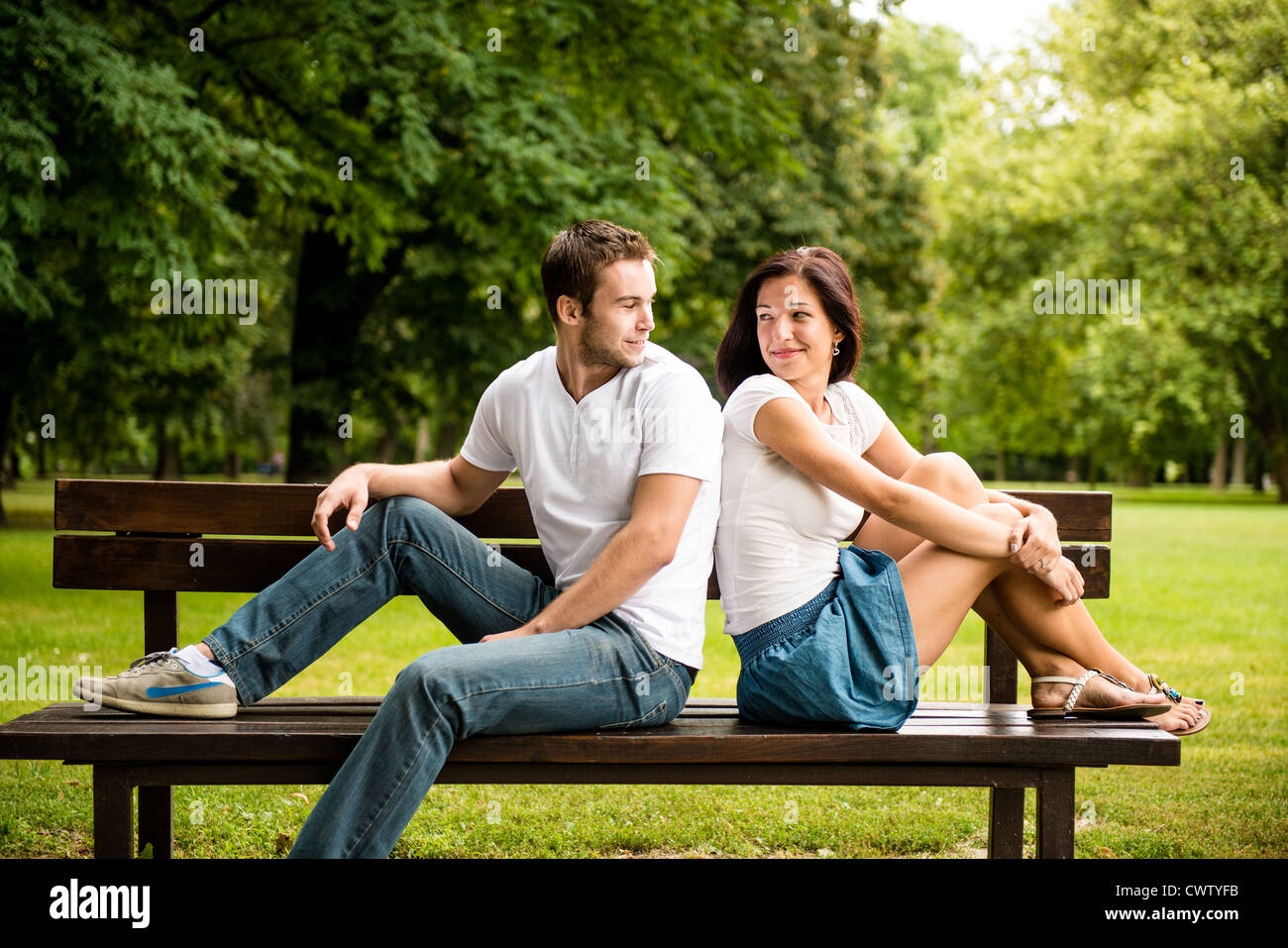 Junges Lächeln paar suchen auf einander - auf Bank sitzend Stockfoto