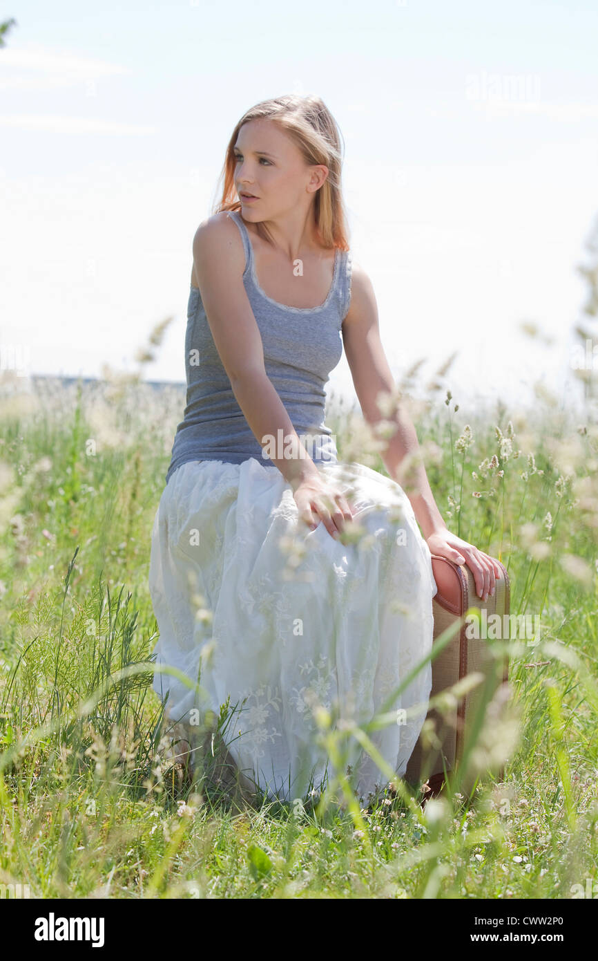 Blonde junge Frau mit Koffer im Feld Stockfoto