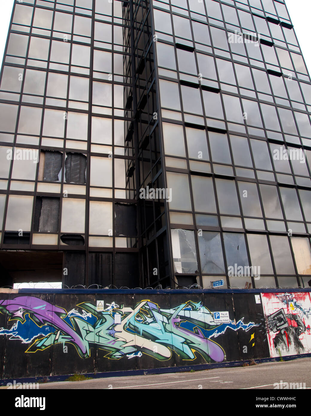 Graffiti-Kunst auf Boardings, die eine geschlossene, Büro-Hochhaus mit zertrümmerten Fenstern in Portsmouth, England umgeben Stockfoto