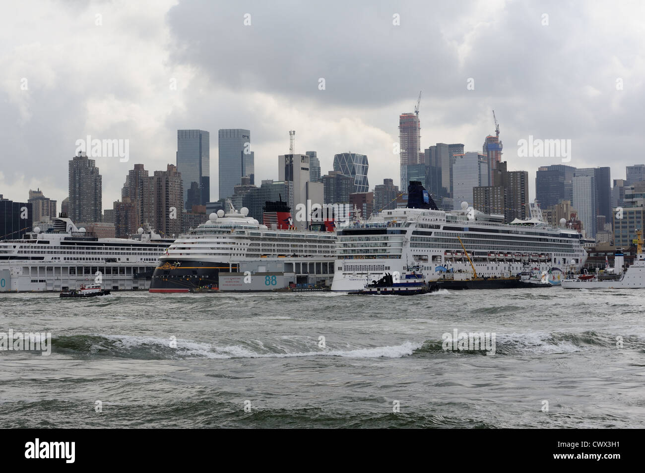 Eine Prozession von Schleppern, vorbei an der Manhattan Cruise Terminal mit drei Kreuzfahrtschiffe im Hafen. Stockfoto