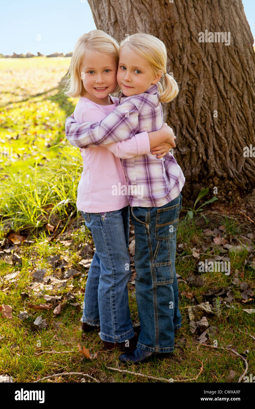 Zwei blonde Mädchen stehen neben einander vor einen Baum. Stockfoto