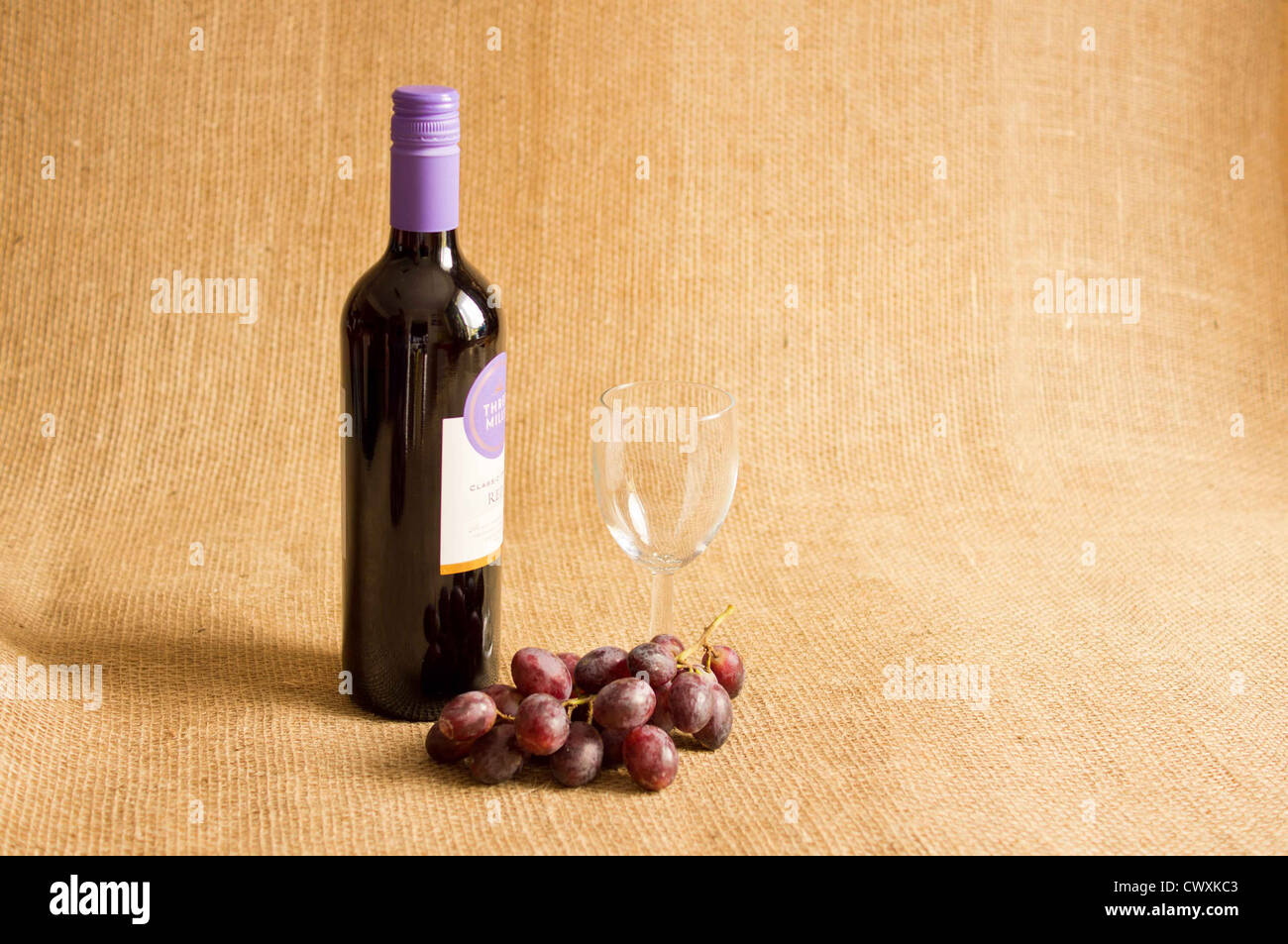 Flasche Rotwein mit einem leeren Glas mit roten Trauben auf eine hessische Hintergrund geschlossen. Stockfoto