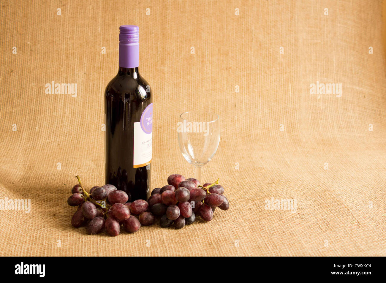Flasche Rotwein mit einem leeren Glas mit roten Trauben auf eine hessische Hintergrund geschlossen. Stockfoto