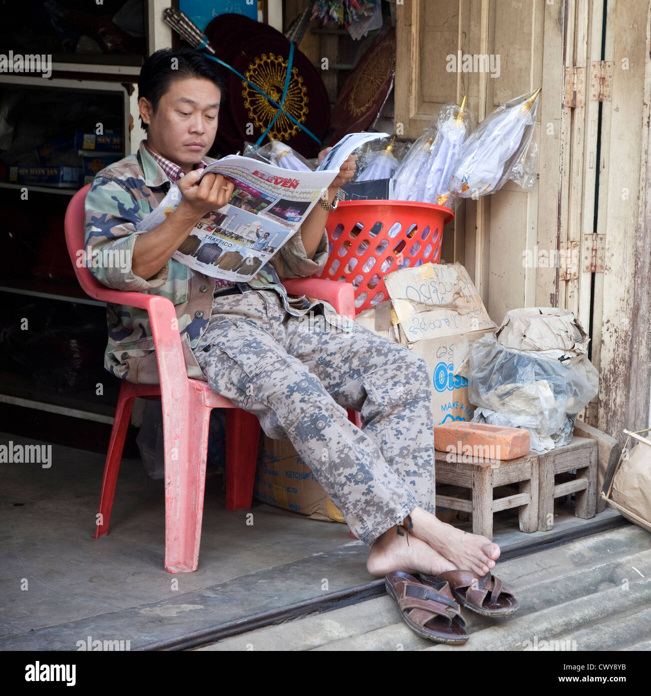 Myanmar, Burma. Mandalay. Burmesische Mann lesen Zeitung. Stockfoto