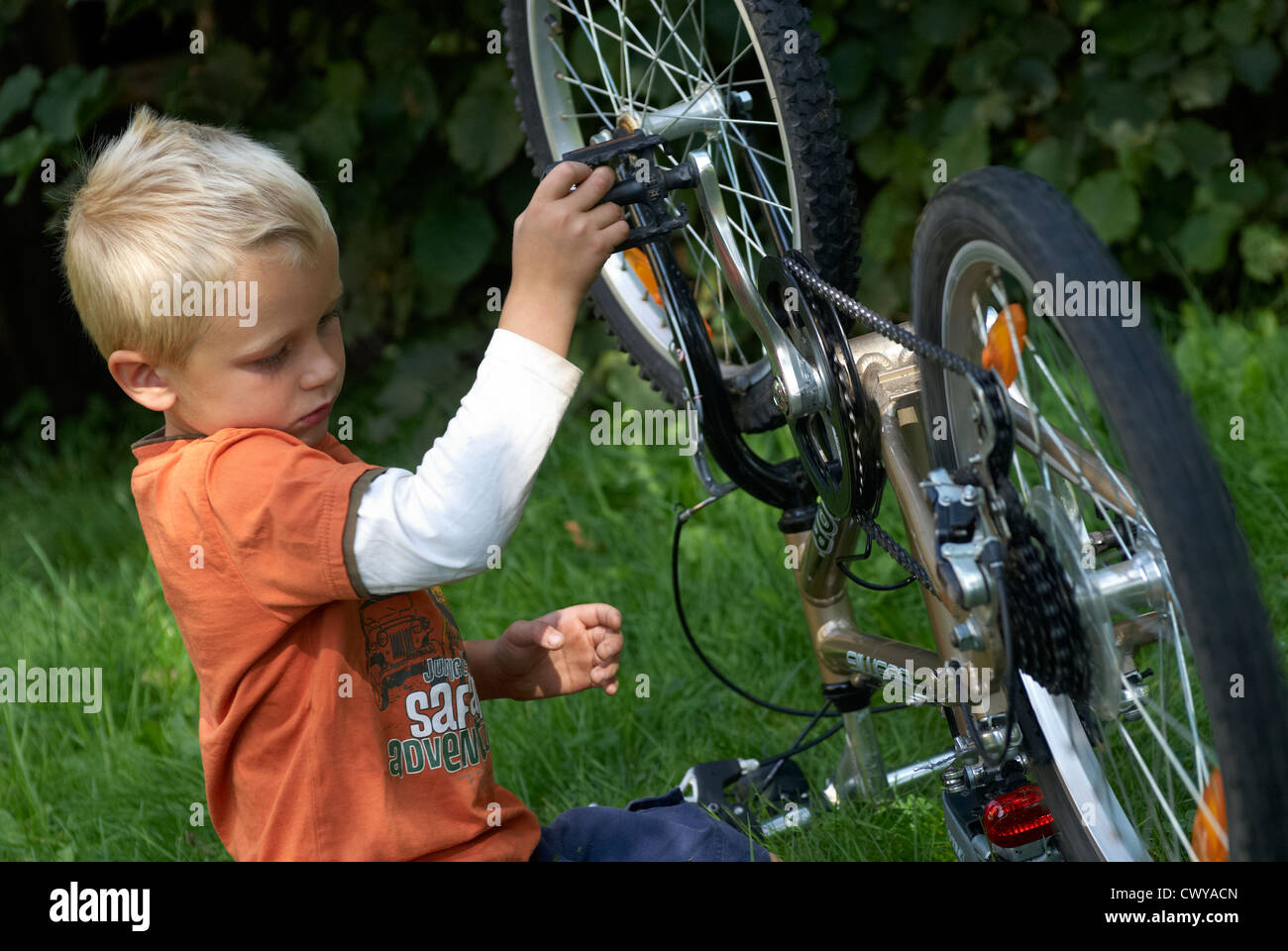 Kind blonde junge Prüfung und Festsetzung seines Fahrrades außerhalb Sommer Stockfoto