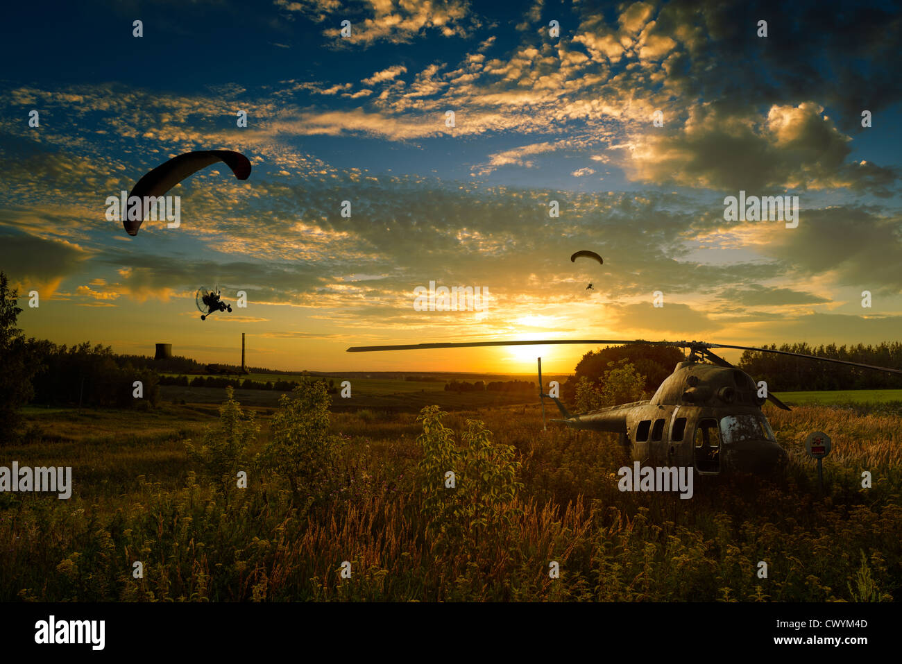 Hubschrauber abgestürzt in den Feldern und Gleitschirme fliegen in Sonnenuntergang. Stockfoto
