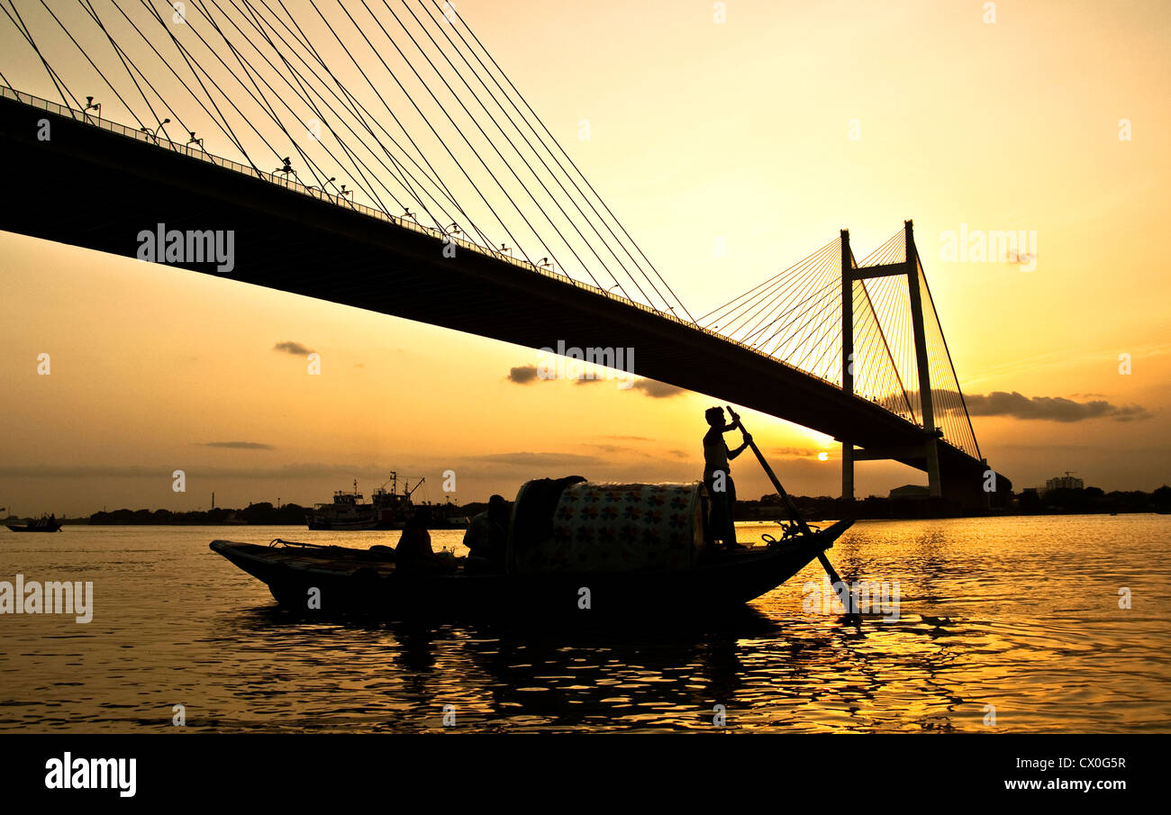 Ein Bootsmann segelt sein Boot bei Sonnenuntergang über dem Fluss Ganges in West Bengalen, Indien. Stockfoto