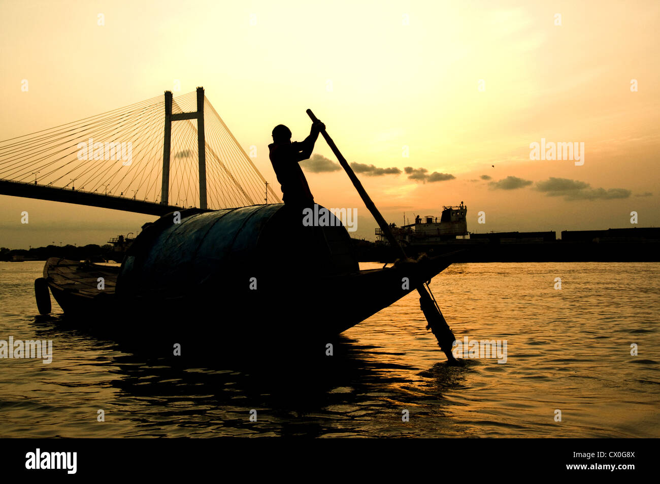 Ein Bootsmann segelt sein Boot bei Sonnenuntergang auf dem Fluss Ganges in Kalkutta, Indien. Stockfoto