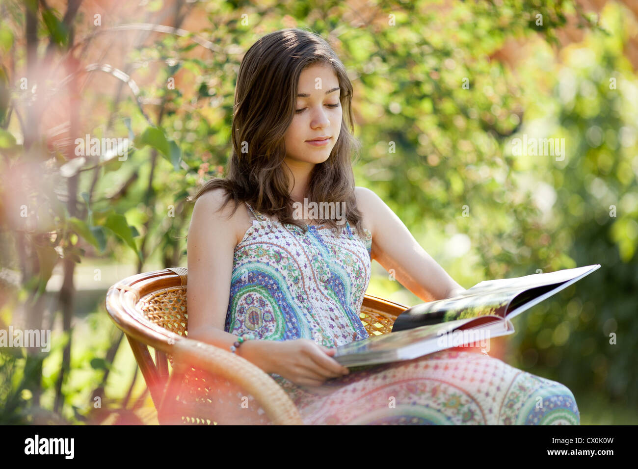 Mädchen lesen Buch im Korbstuhl in Sommertag im Freien sitzen Stockfoto