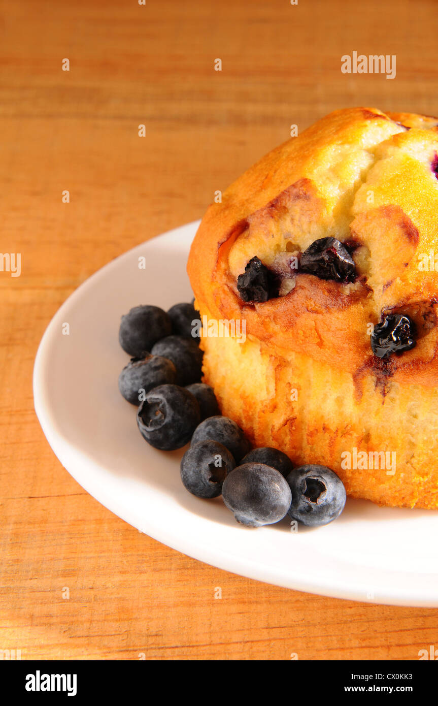 Nahaufnahme einer Blueberry Muffin und lose Beeren auf einem weißen Teller auf einem rustikalen Holztisch. Stockfoto