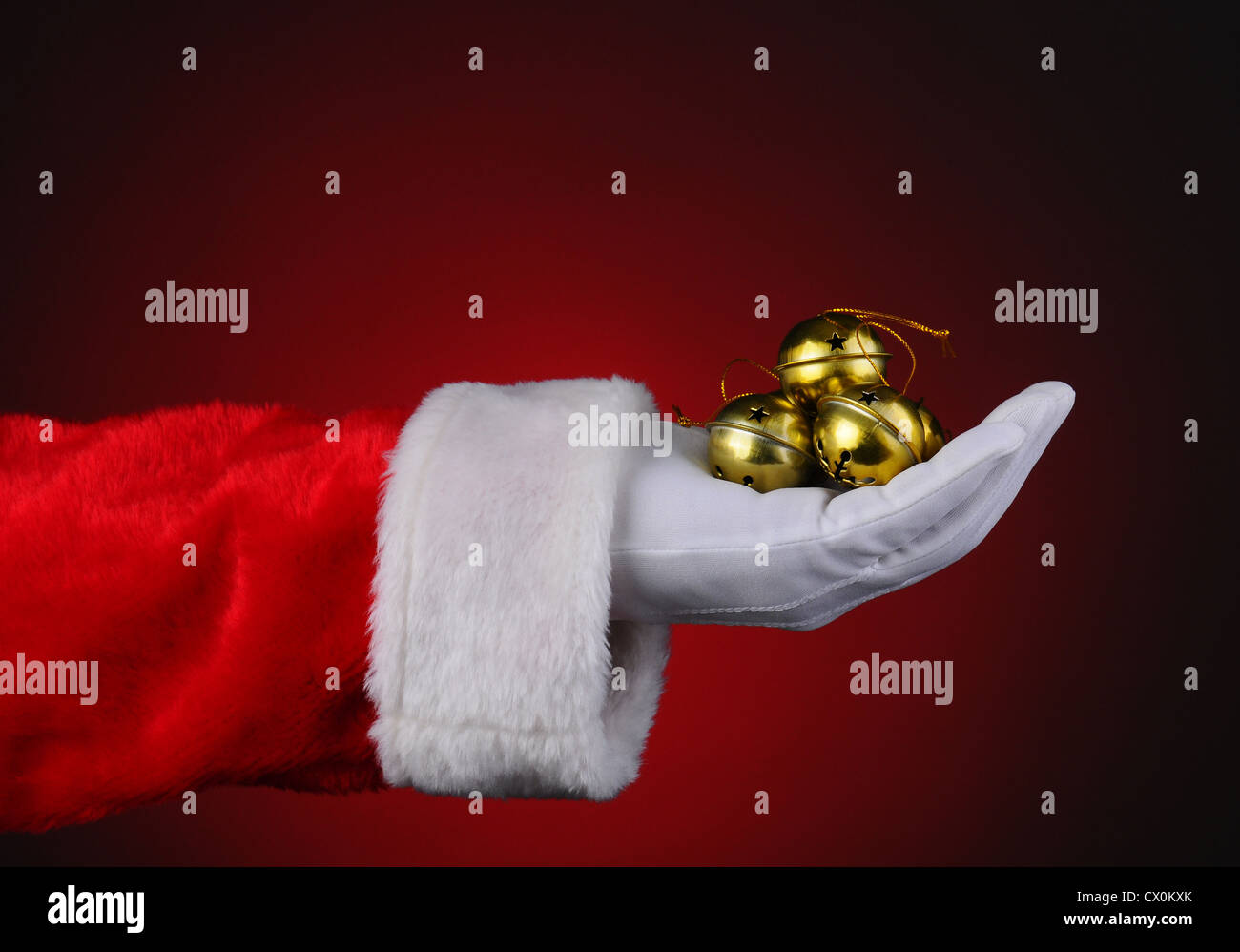 Santa Claus mit einer Handvoll goldene Glöckchen über ein rotes Licht auf dunklem Hintergrund. Stockfoto
