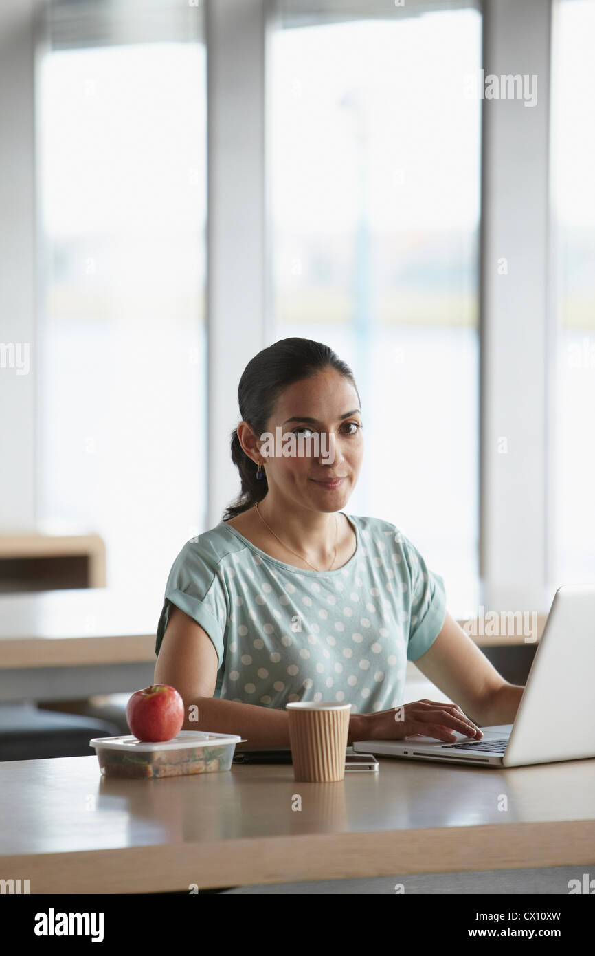Frau mit Laptop mit Lunchpaket auf Schreibtisch Stockfoto