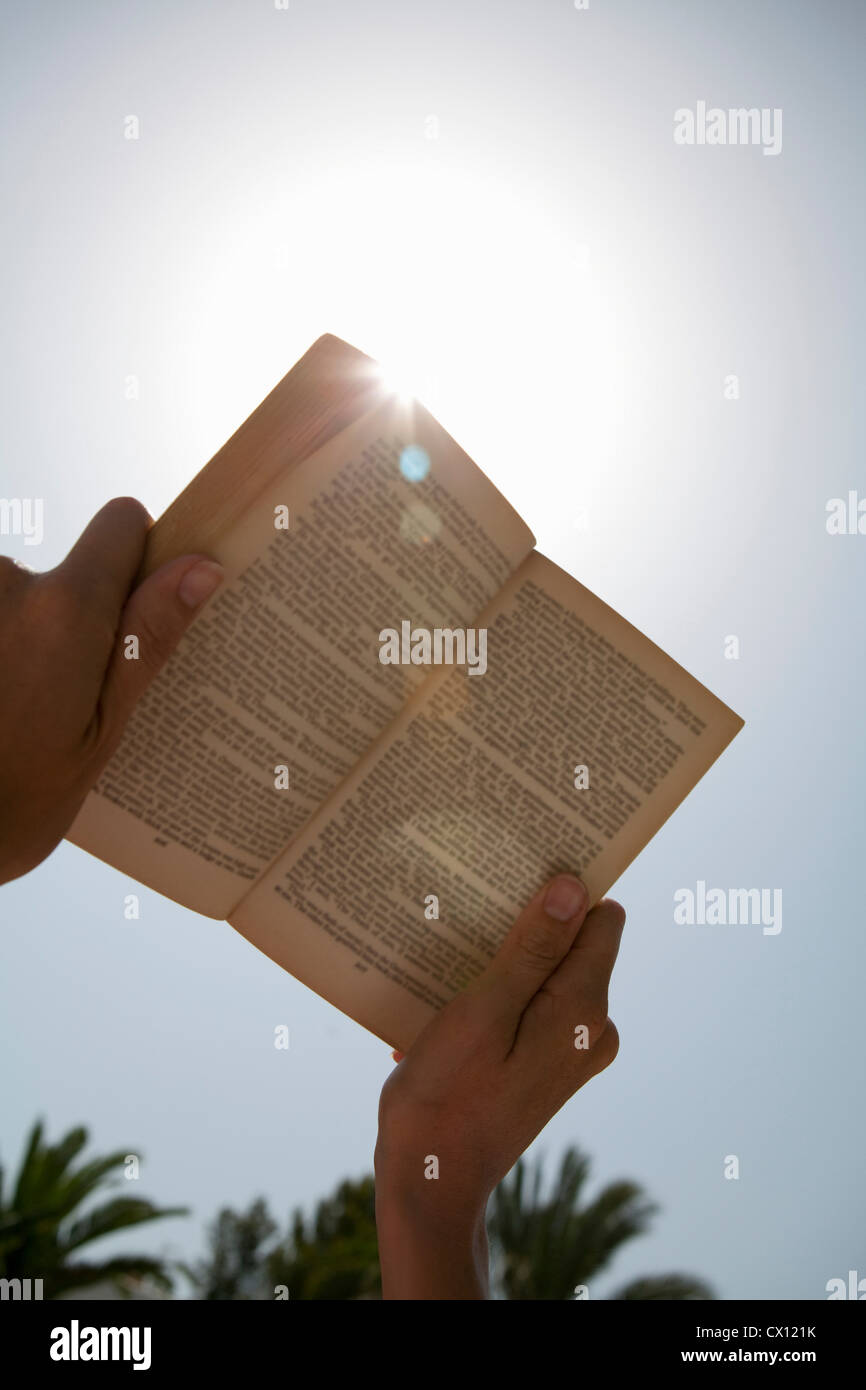 Person hält Buch gegen die Sonne Stockfoto