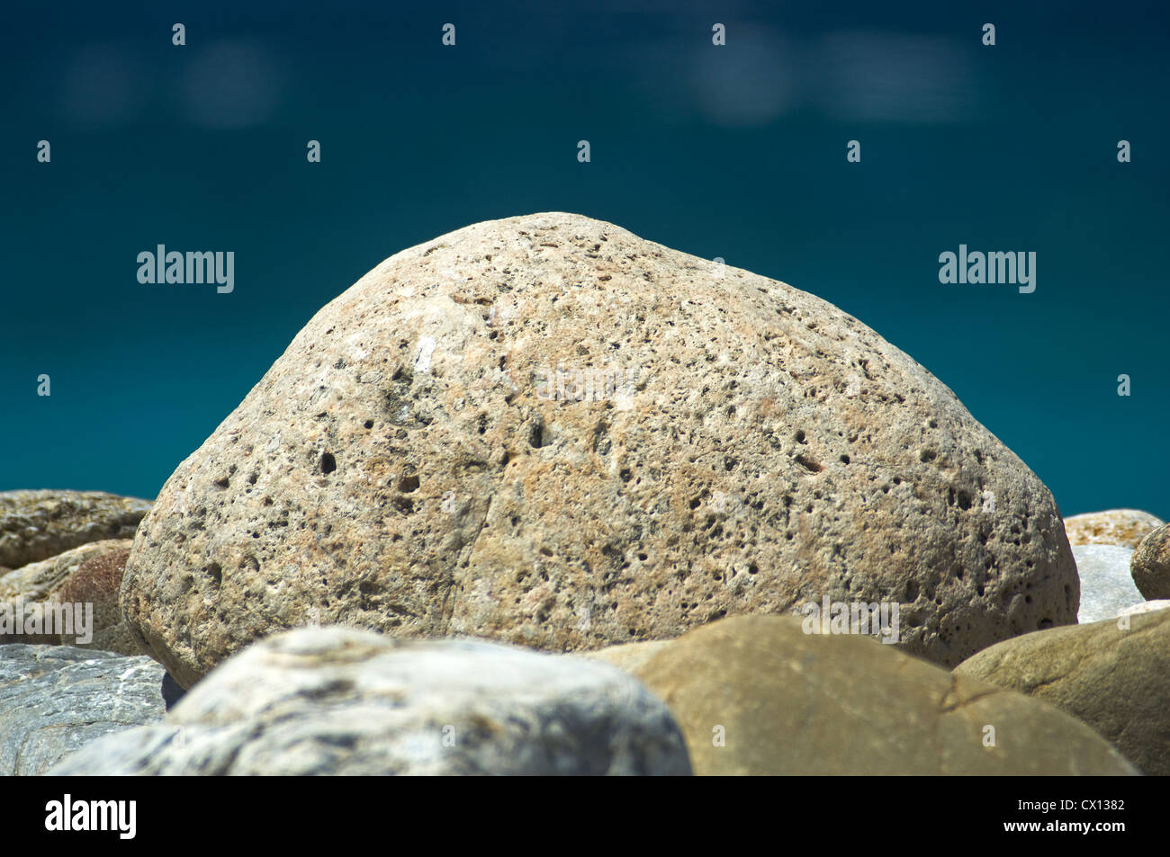 Nahaufnahme von einem großen Kieselstein auf einem Kiesstrand mit dem blauen Meer im Hintergrund Stockfoto