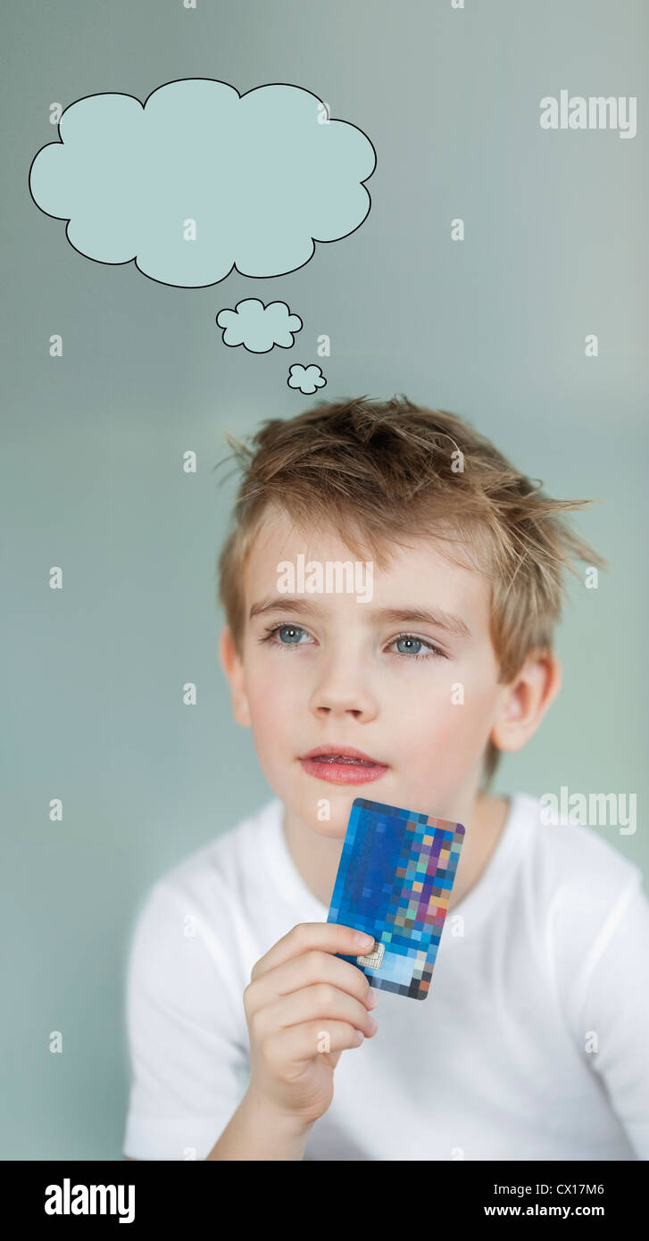 Nachdenkliche kleine Junge Holding Kreditkarte mit Rede bubble über grauen Hintergrund Stockfoto