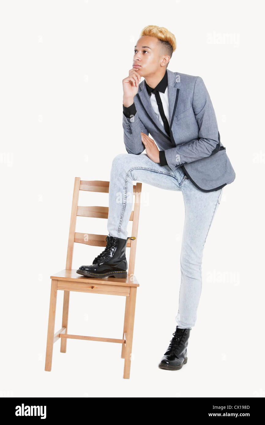 Nachdenklich Teenager steht mit einem Bein auf Stuhl über grauen Hintergrund Stockfoto