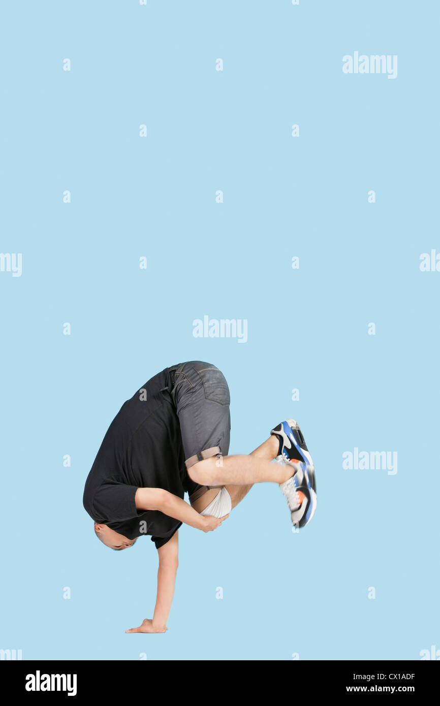 Männliche Break Dancer balanciert auf dem Kopf stehend auf der einen Seite über blauen Hintergrund Stockfoto