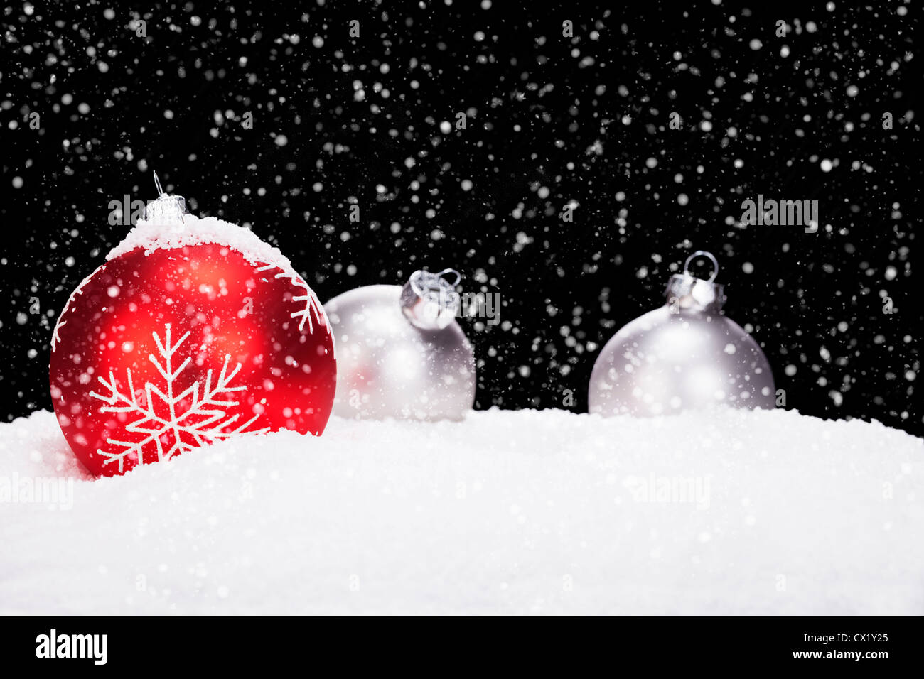 rote und silberne Weihnachtskugeln im Schnee auf schwarzem Hintergrund während schneit Stockfoto