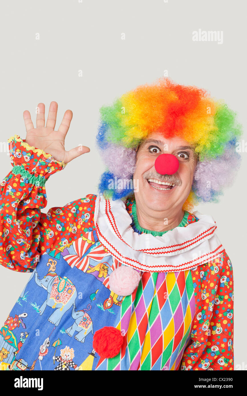 Porträt von fröhlichen senior männlichen Clown winken Hand über grauen Hintergrund Stockfoto