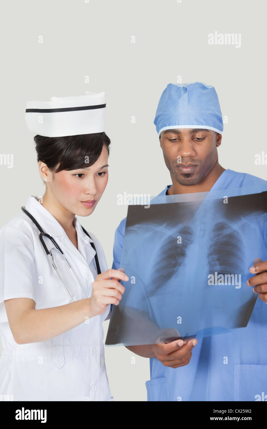 Männliche Chirurgen mit Krankenschwester Untersuchung Röntgen-Bericht über grauen Hintergrund Stockfoto