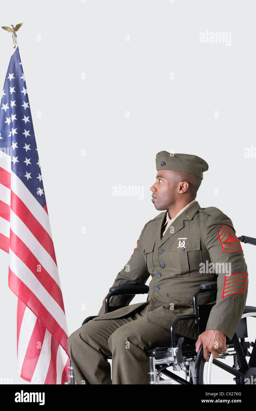 Jung uns Soldat im Rollstuhl Blick auf amerikanische Flagge über dem grauen Hintergrund Stockfoto