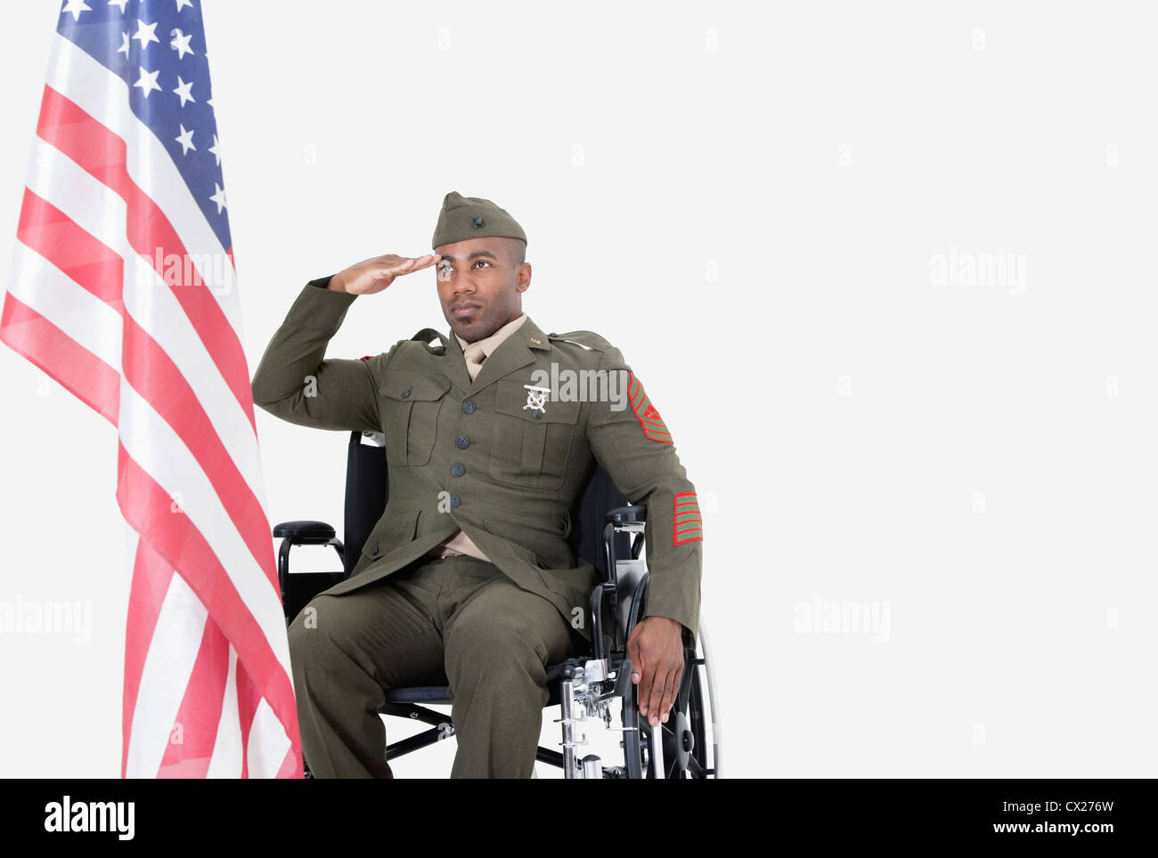 Jung uns Soldat im Rollstuhl, die amerikanische Flagge über dem grauen Hintergrund grüßen Stockfoto