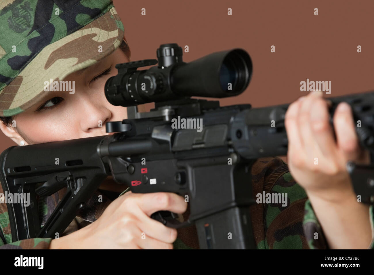 Junge Soldatin US Marine Corps mit dem Ziel M4-Sturmgewehr auf braunem Hintergrund Stockfoto