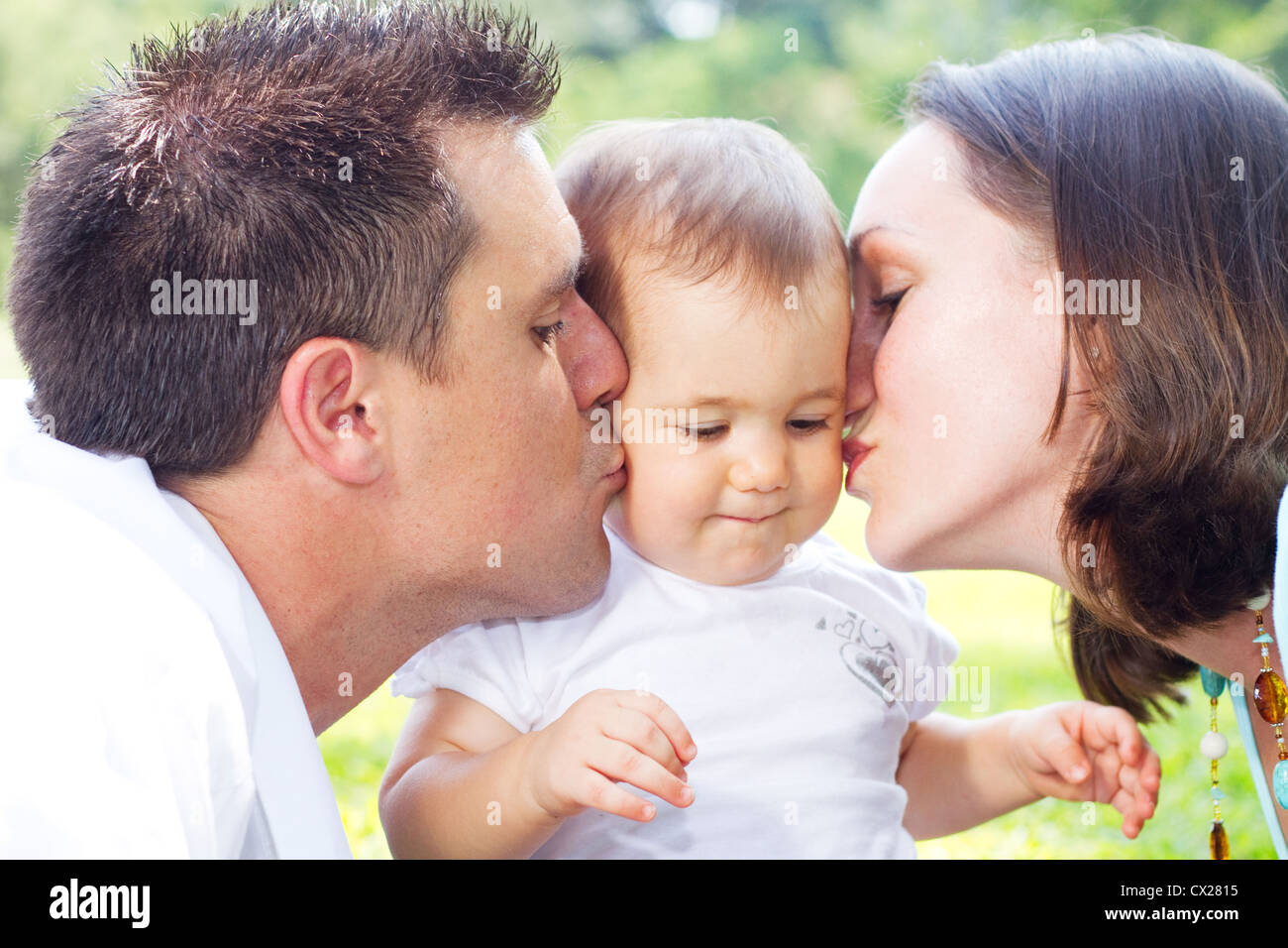 Eltern küssen Babymädchen im freien Stockfoto