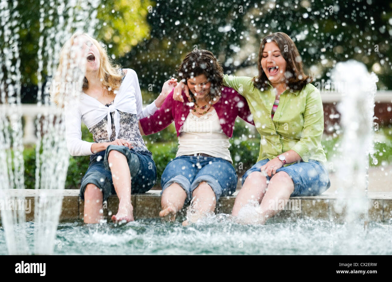 Drei Mädchen sitzen auf dem Rand eines Brunnens lachend, als sie ihre Füße in das Wasser tauchen. Stockfoto