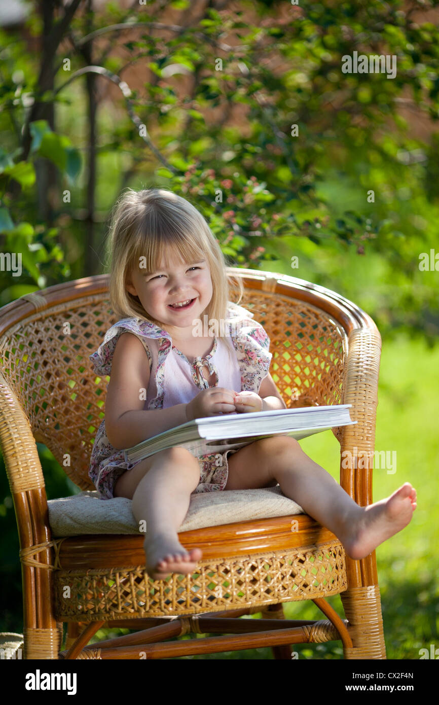 Kleines Mädchen Buch im Korbstuhl in Sommertag im Freien sitzen Stockfoto