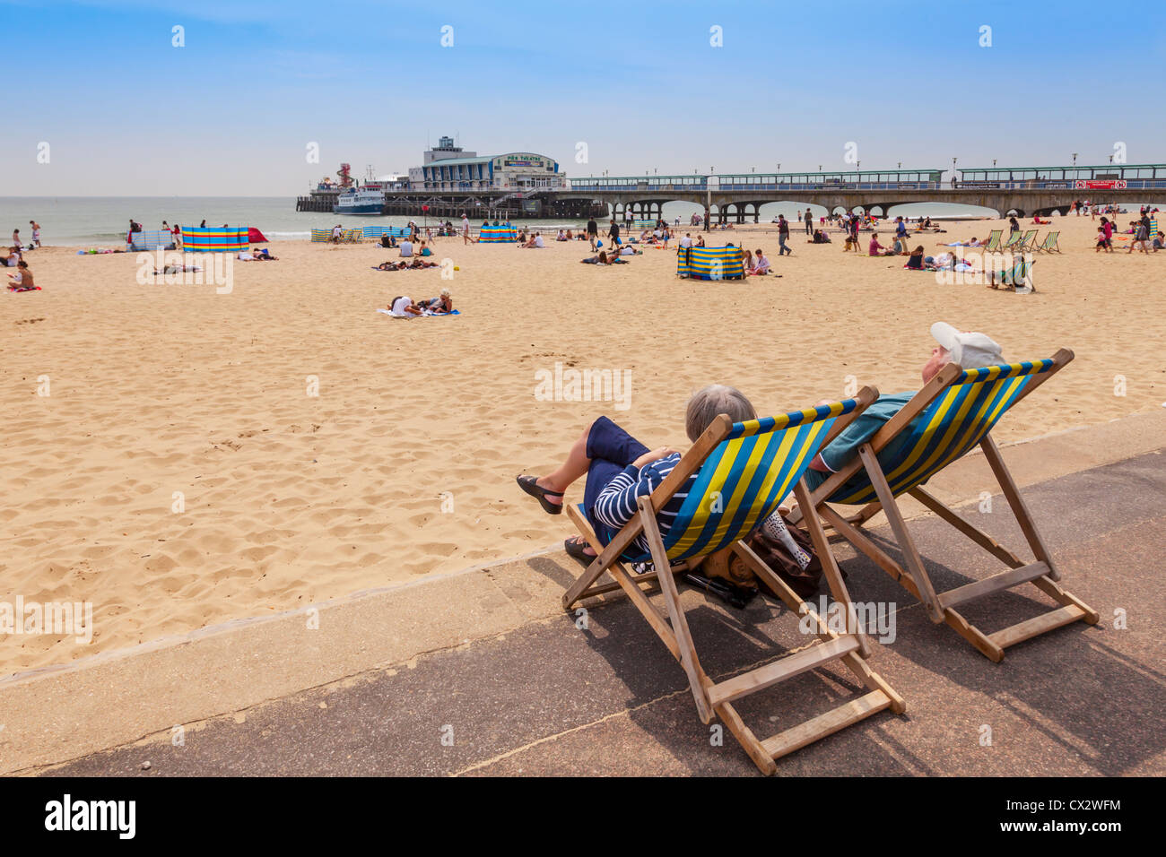 Älteres paar sitzen in Liegestühlen mit Blick auf Bournemouth Strand und Pier, Dorset, England. Stockfoto