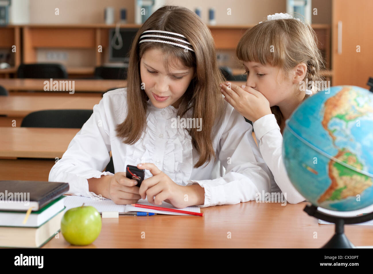 Zwei Mädchen sitzen am Schreibtisch mit Handy Stockfoto