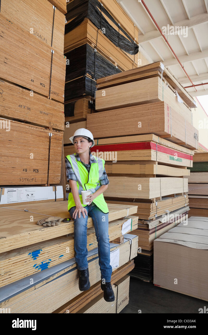 Industrielle Arbeitnehmerin Kaffeetrinken beim Sitzen auf Stapel von Holzbohlen Stockfoto