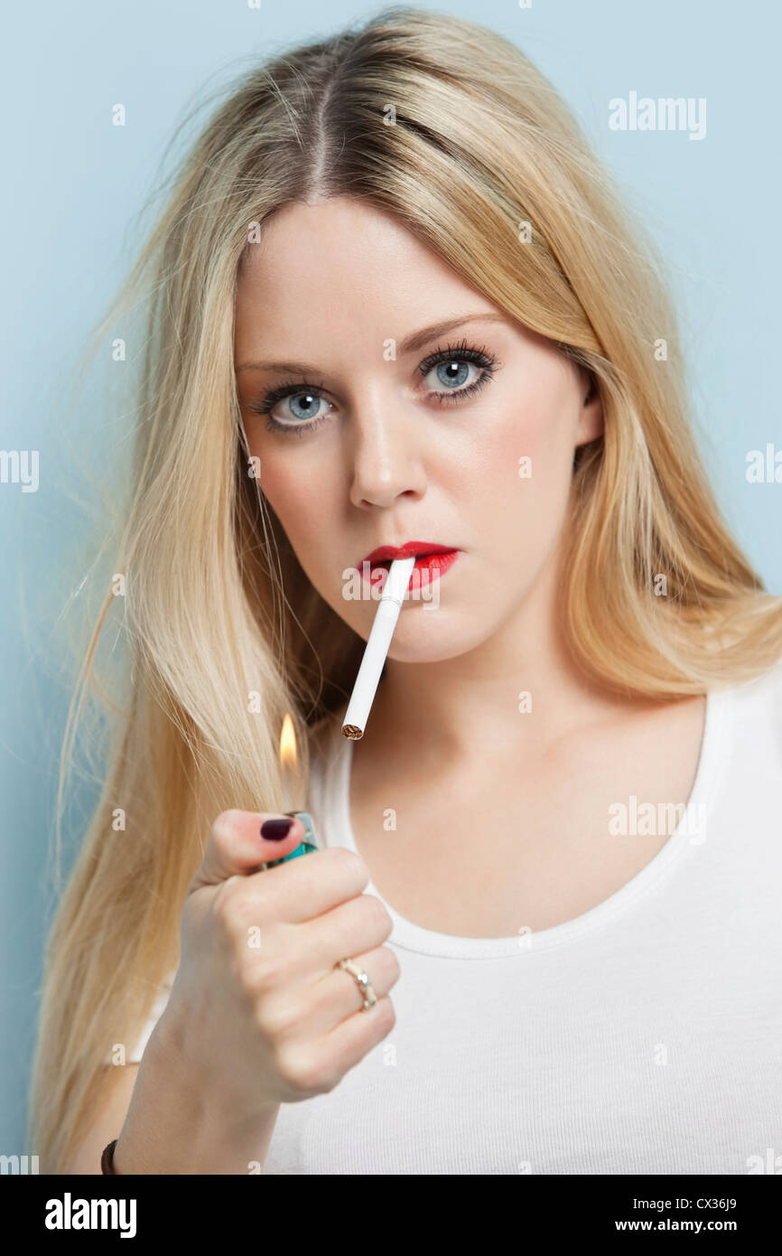 Porträt der jungen blonden Frau zünden Zigarette vor hellblauem Hintergrund Stockfoto