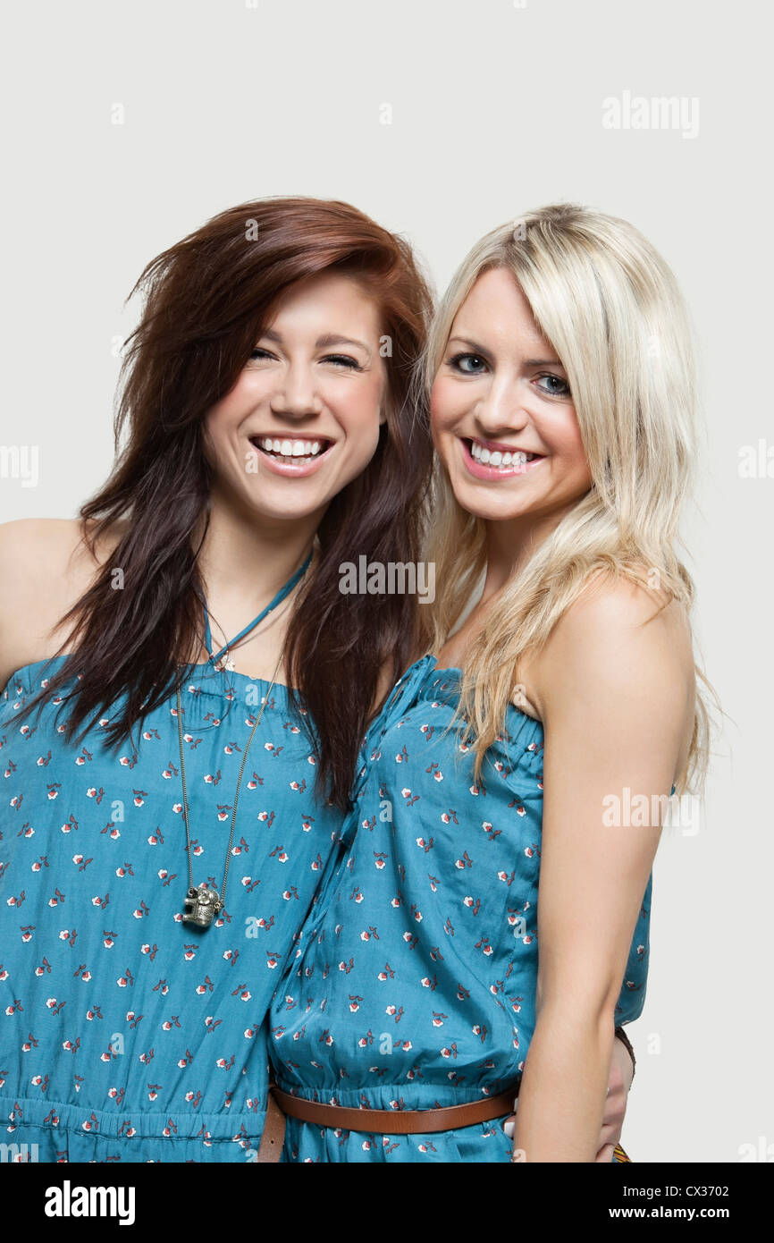 Porträt zweier junger Frauen in ähnlichen Overalls lächelnd über grauen Hintergrund Stockfoto