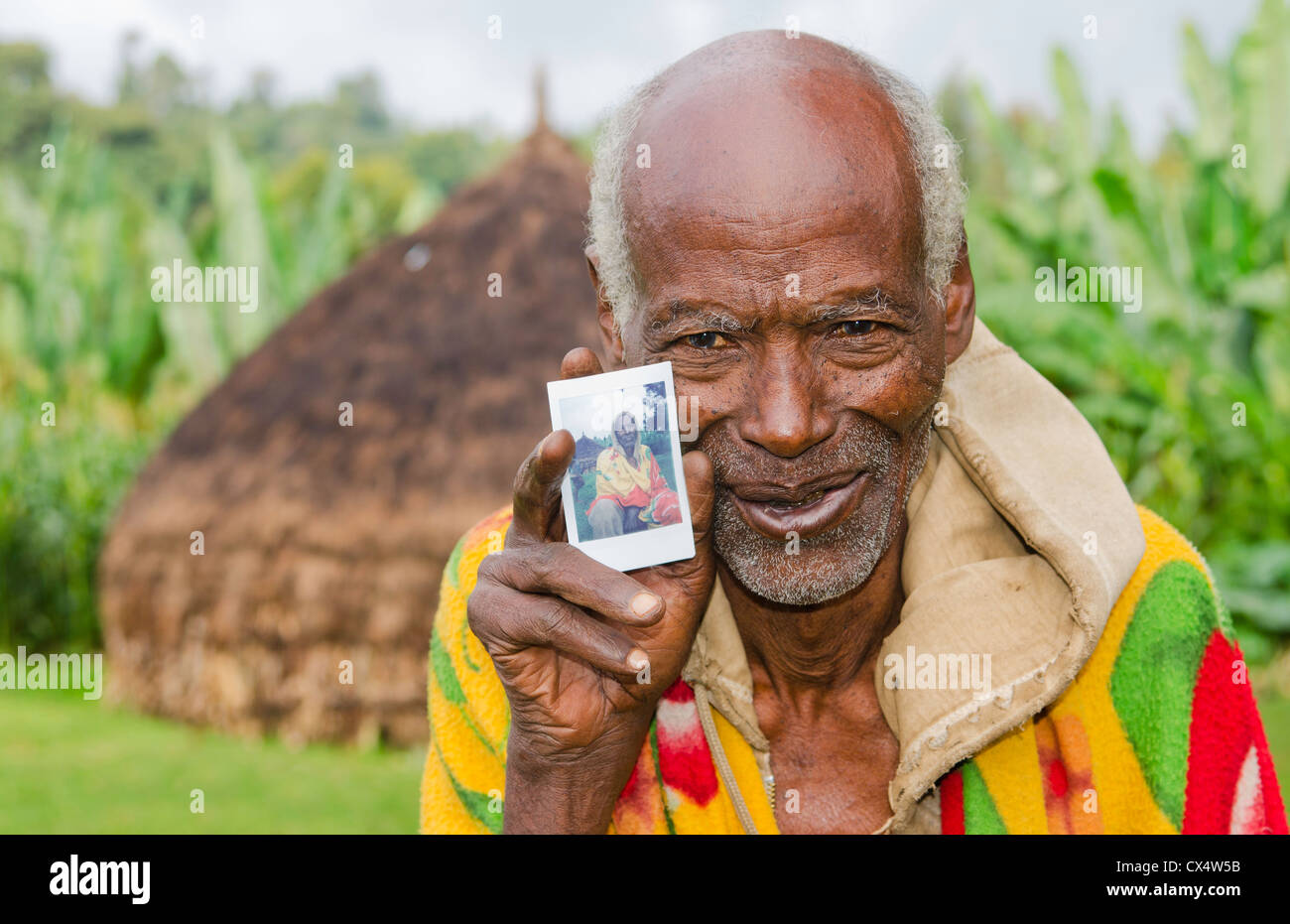 Sidama Stamm Äthiopien Afrika Greis Alter von 82 Jahren mit seinem Haus Hütte und hält neue Fuji Polaroid photo print #30 Stockfoto