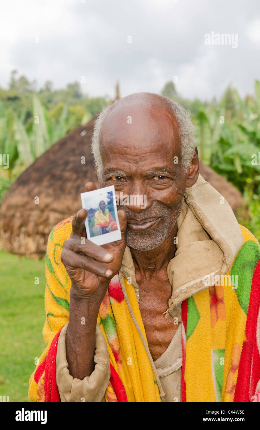 Sidama Stamm Äthiopien Afrika Greis Alter von 82 Jahren mit seinem Haus Hütte und hält neue Fuji Polaroid photo print #30 Stockfoto