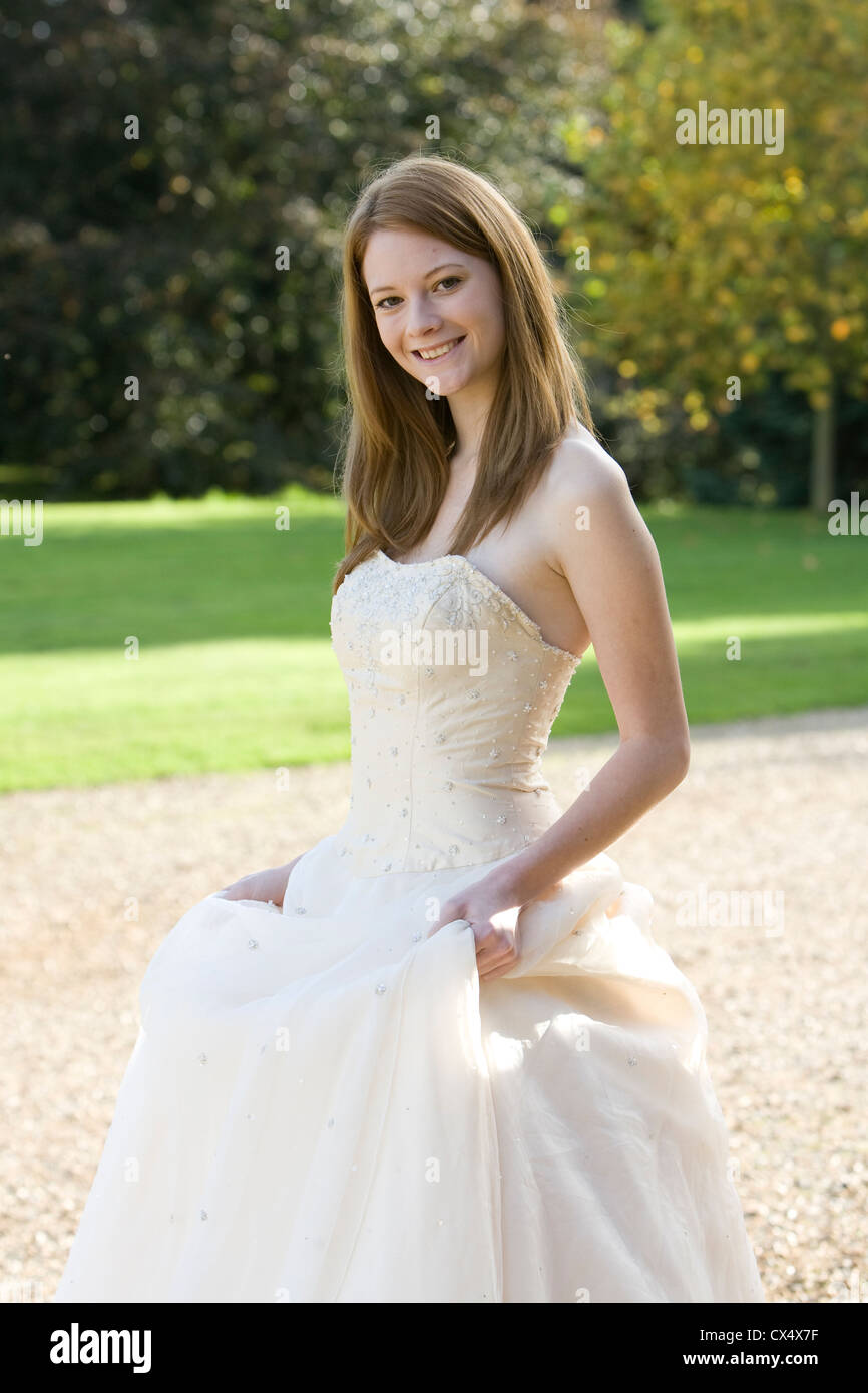 Junge Frau in Creme trägerlosen Brautkleid hält Röcke im Garten des Herrenhauses Stockfoto