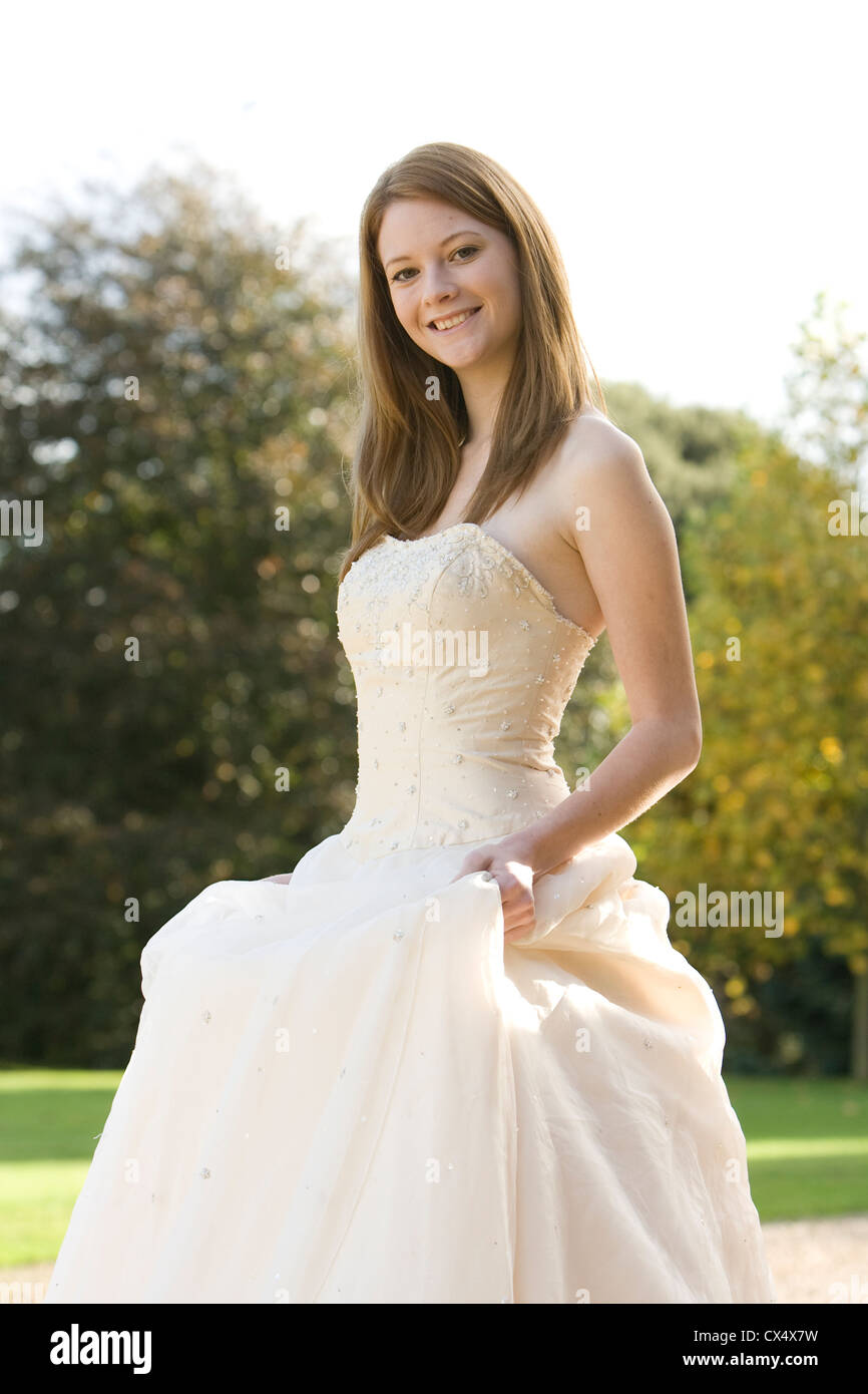 Junge Frau in Creme trägerlosen Brautkleid hält Röcke im Garten des Herrenhauses Stockfoto