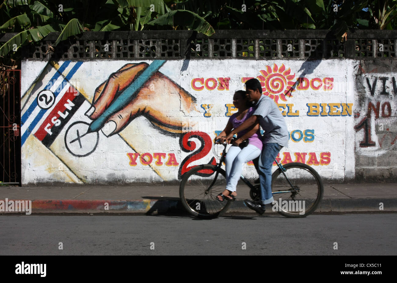 Mann und Frau fahren mit dem Fahrrad am Sandinista-Wahlschild in Ometepe Nicaragua vorbei Stockfoto