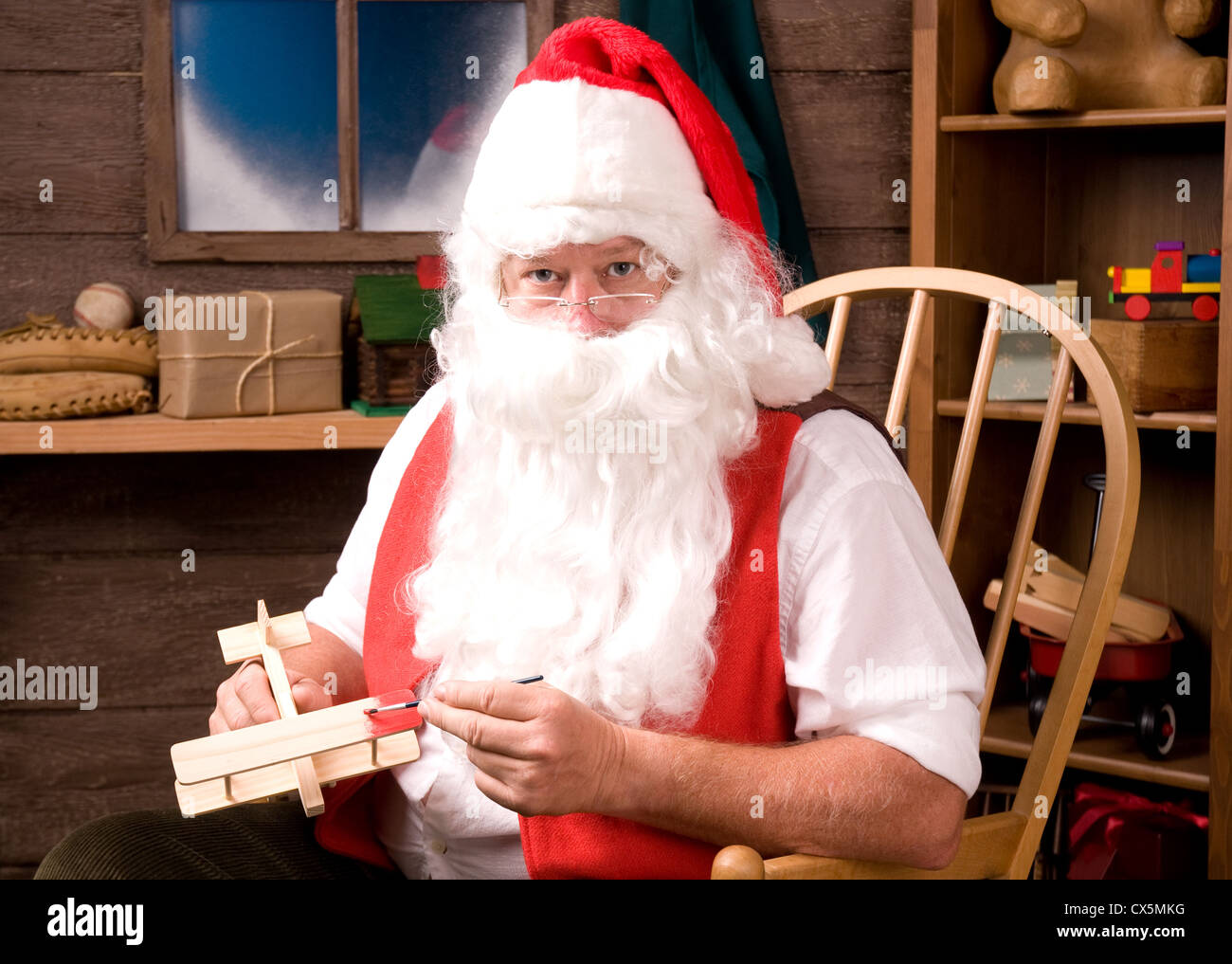 Weihnachtsmann sitzt im Schaukelstuhl in seiner Werkstatt malen ein Spielzeugflugzeug. Horizontale Komposition. Stockfoto