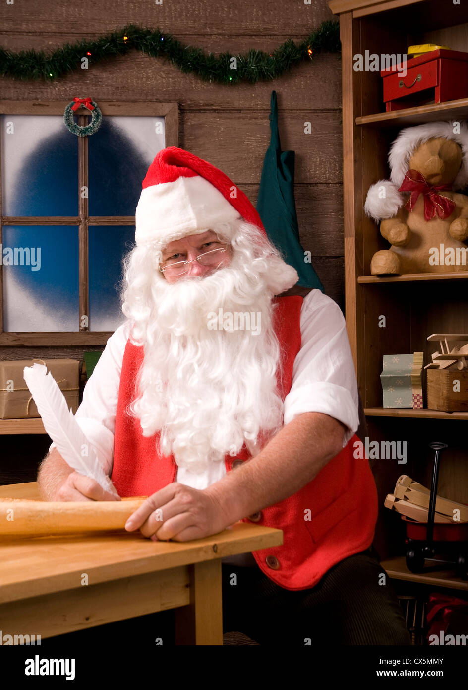 Weihnachtsmann sitzt in seiner Werkstatt mit Feder Stift schreiben auf seiner Liste. Vertikale Zusammensetzung. Stockfoto